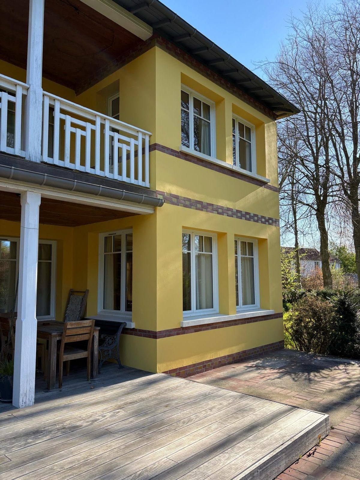 Façade jaune repeinte avec encadrements clairs et balcon